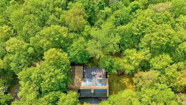 Vista aérea de um edifício moderno e retangular, rodeado por uma floresta verde densa.