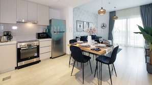 Une cuisine moderne dotée d’appareils électroménagers intégrés, un coin repas avec une table dressée pour quatre personnes et une grande fenêtre agrémentée de rideaux.