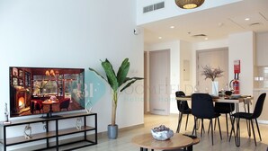 Un salon moderne avec un grand téléviseur, une plante en pot et un coin repas comprenant une table et des chaises.