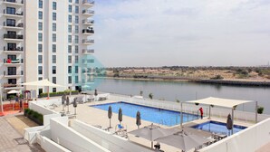 Une piscine sur le toit, offrant une vue sur une rivière, et entourée d’un bâtiment blanc doté de balcons.