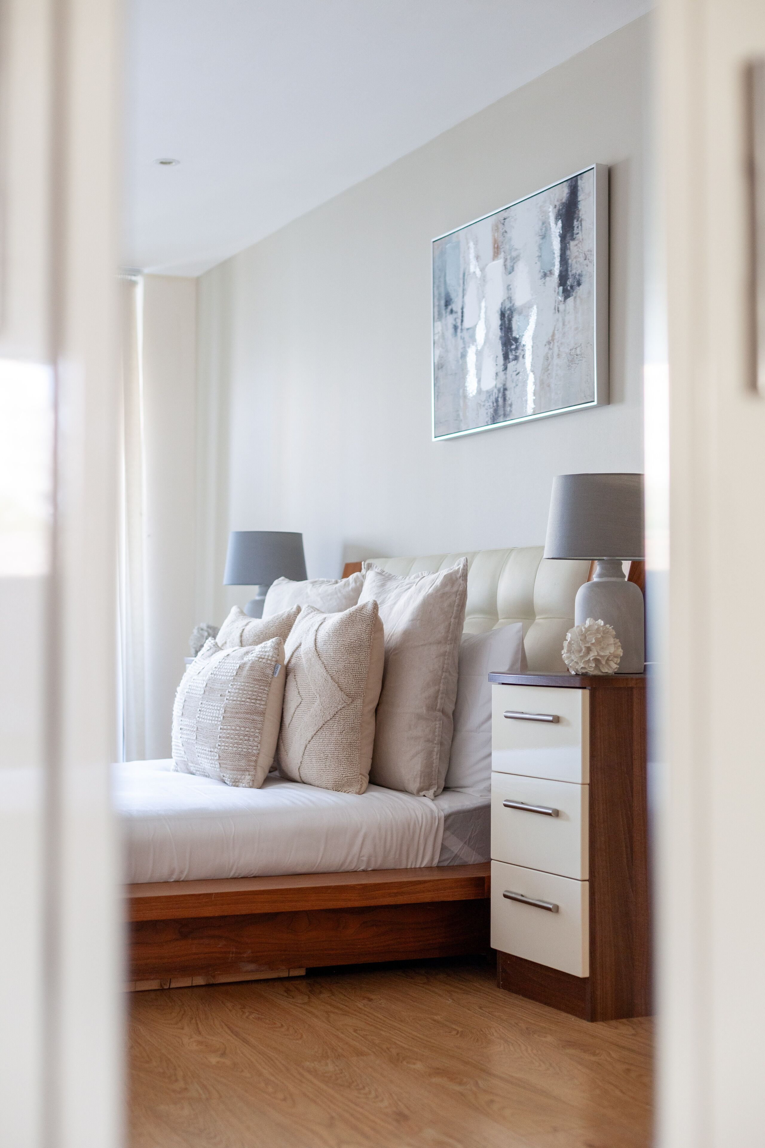 Un dormitorio con cama, mesitas de noche, una lámpara y un cuadro en la pared.
