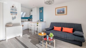 Ein modernes Wohnzimmer mit einem grauen Sofa, einem kleinen runden Tisch und einer Küche im Hintergrund.