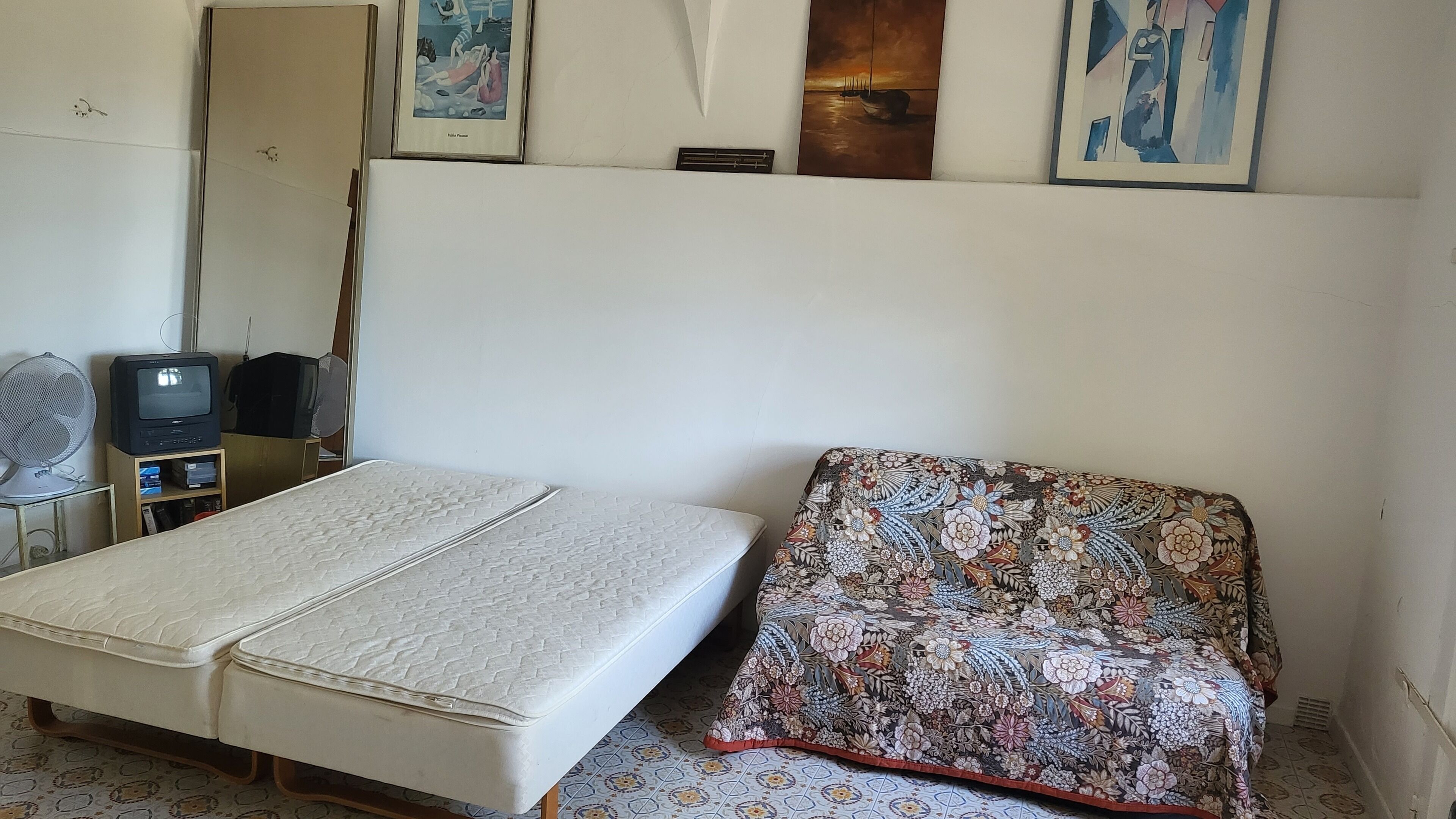 A room with a bed, a television, and a fan.