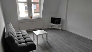 A modern living room with a grey sofa, a white coffee table, and a TV on a white stand. - Beautiful apartment on the roof floor for 5 people (Zeitz)