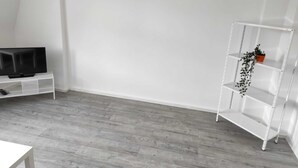 A room with a white TV stand, a white shelving unit, and a grey wooden floor. - Beautiful apartment on the roof floor for 5 people (Zeitz)