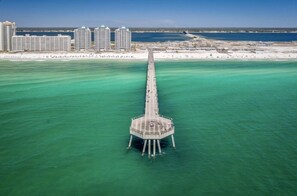 Vista aérea de un muelle que se adentra en aguas turquesas, con un complejo hotelero al fondo.