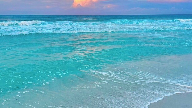 Uma praia com águas turquesa cristalinas e um céu ao pôr do sol.