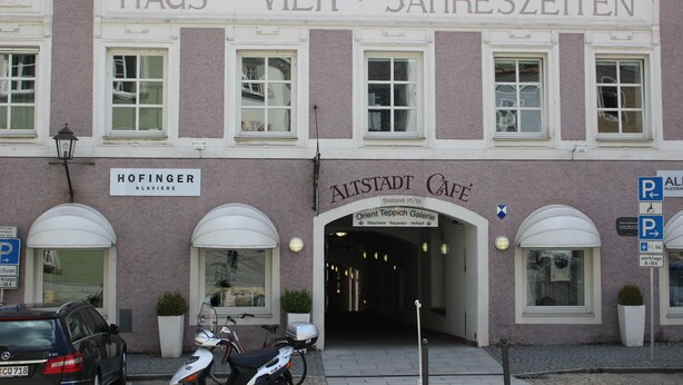 A building with a sign reading "HAUS VIER JAHRESZEITEN" and another sign for "ALTSTADT CAFÉ". There are parked cars and a motorcycle in front. - ZV-Scholtz Burghausen Stadtplatz 95 (Burghausen)