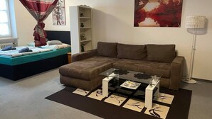 A modern living room with a brown sectional sofa, a glass coffee table, and a bed with a striped canopy. - ZV-Scholtz Burghausen Stadtplatz 95 (Burghausen)