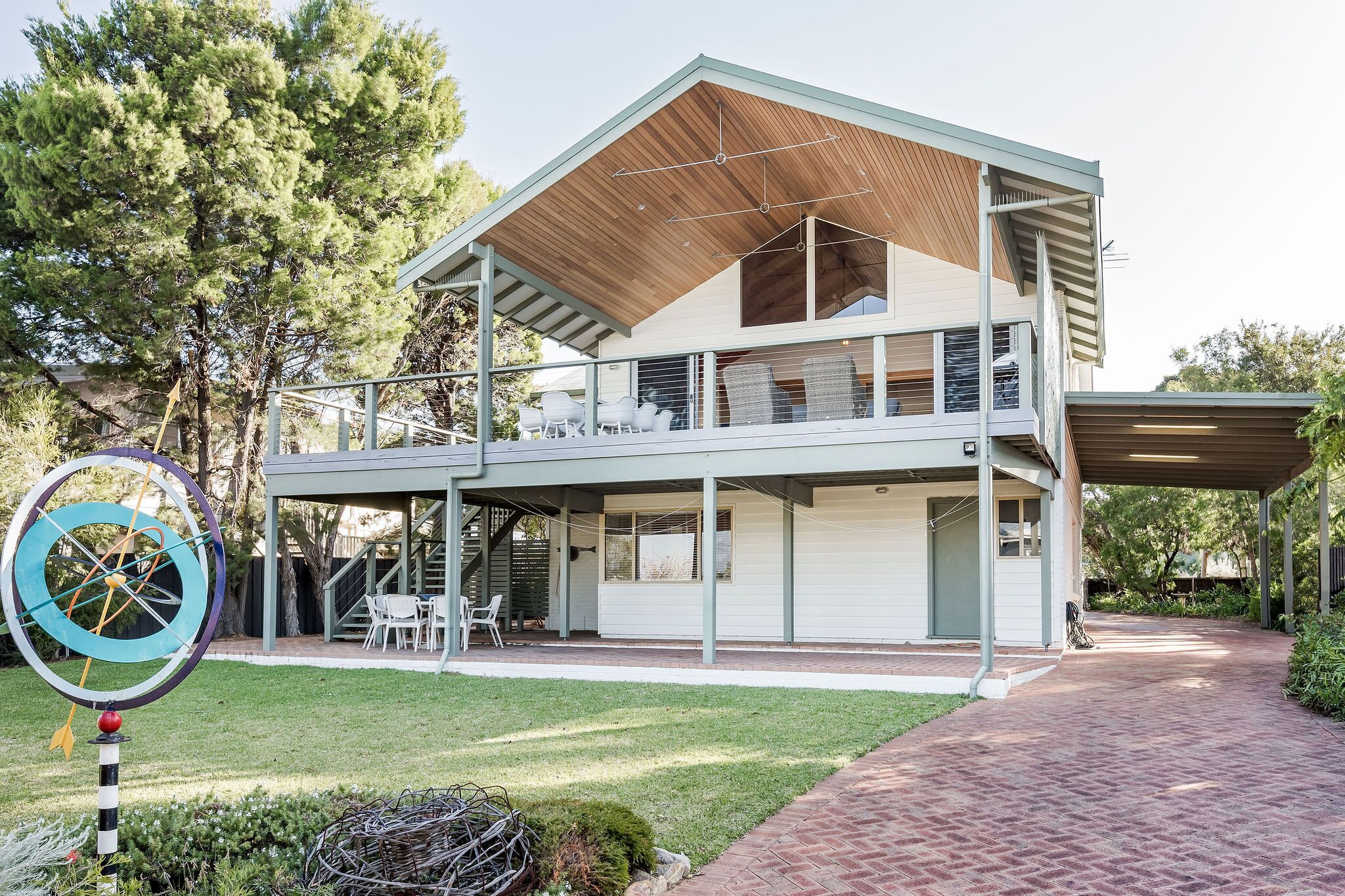 A two-story modern house with a covered patio, a visible staircase, and a large tree in the background.