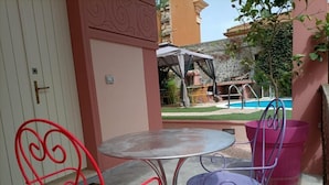 A patio with two metal chairs, a round table, and a pool in the background. - Downtown poolfront room with private veranda (Oristano)