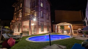 A multi-story building with a swimming pool, outdoor seating, and a covered area with lighting. - Downtown poolfront room with private veranda (Oristano)