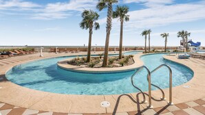 A pool area with palm trees, lounge chairs, and a water slide. - Phoenix Orange Beach!  Lazy River and Slide !  New Rental!! (Orange Beach)