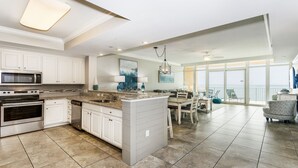 A spacious kitchen with white cabinetry, a central island, and a dining area with a view of the ocean. - Phoenix Orange Beach!  Lazy River and Slide !  New Rental!! (Orange Beach)