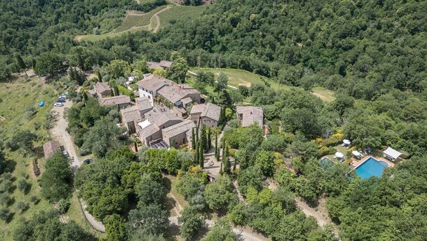Luftfoto af en landlig landsby med stenhuse, en swimmingpool og frodig vegetation omkring.