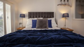 A bedroom with a large bed, two bedside tables, a window with blinds, and a decorative wall piece. - Pretty dog friendly cottage for two in the heart of the Georgian town of Richmond, North Yorkshire (Richmond)
