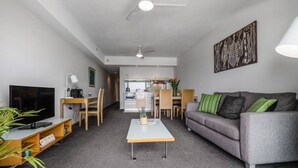Ett modernt vardagsrum med en grå soffa, ett soffbord, en tv och en matplats med stolar och ett bord.
