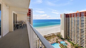 Ein Balkon mit Tisch und Stühlen, mit Blick auf einen Strand und ein Schwimmbad.