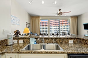 A kitchen with granite countertops, a double sink, a ceiling fan, and a view of a high-rise building.