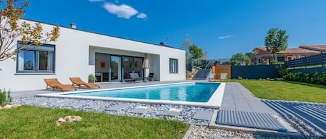 Una casa moderna con piscina, mobiliario exterior y césped cuidado.