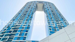 A modern high-rise building with a prominent central atrium. - HomesGetaway-1Bedroom in JBR The Address (Dubai)