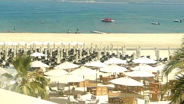 A beachside resort with rows of sun umbrellas and lounge chairs, a sandy beach, and boats in the water. - HomesGetaway-1Bedroom in JBR The Address (Dubai)