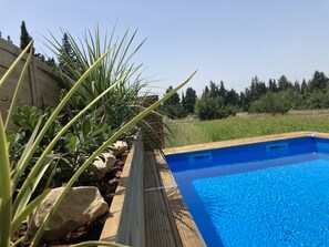 Une piscine dotée d’une terrasse en bois et entourée de verdure.