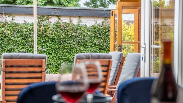 Ein Essbereich im Freien mit Holzkufen und einem Tisch, ein Glas Rotwein und eine Flasche Champagner.