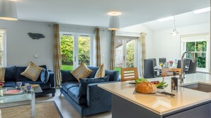 Een moderne woonkamer met een blauwe bank, een glazen salontafel en een keukeneiland met een brood en een mes.