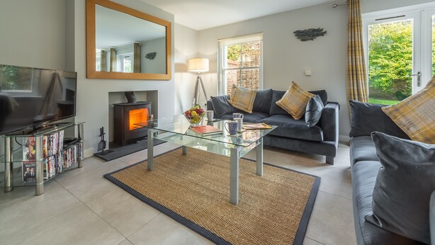 Een moderne woonkamer met een glazen salontafel, grijze banken, een open haard en een grote spiegel.