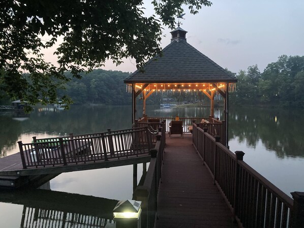 Una glorieta con cubierta y baranda de madera, con vista a un lago tranquilo.