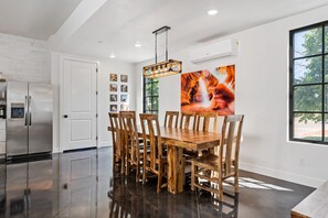 A modern kitchen with a stainless steel refrigerator, a wooden dining table with chairs, and a large window with a view of trees. - The Sand Hollow Retreat: Private Pool, Bbq, Fire Table (Hurricane)