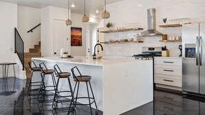 A modern kitchen with a large island, bar stools, stainless steel appliances, and a staircase. - The Sand Hollow Retreat: Private Pool, Bbq, Fire Table (Hurricane)