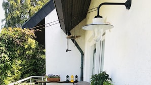 Una terraza de madera con una mesa y sillas, rodeada de follaje y una jardinera.