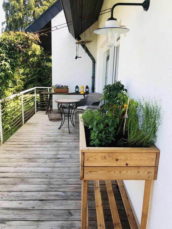 Eine Holzterrasse mit Tisch und Stühlen, umgeben von viel Grün und einer Pflanzkiste.