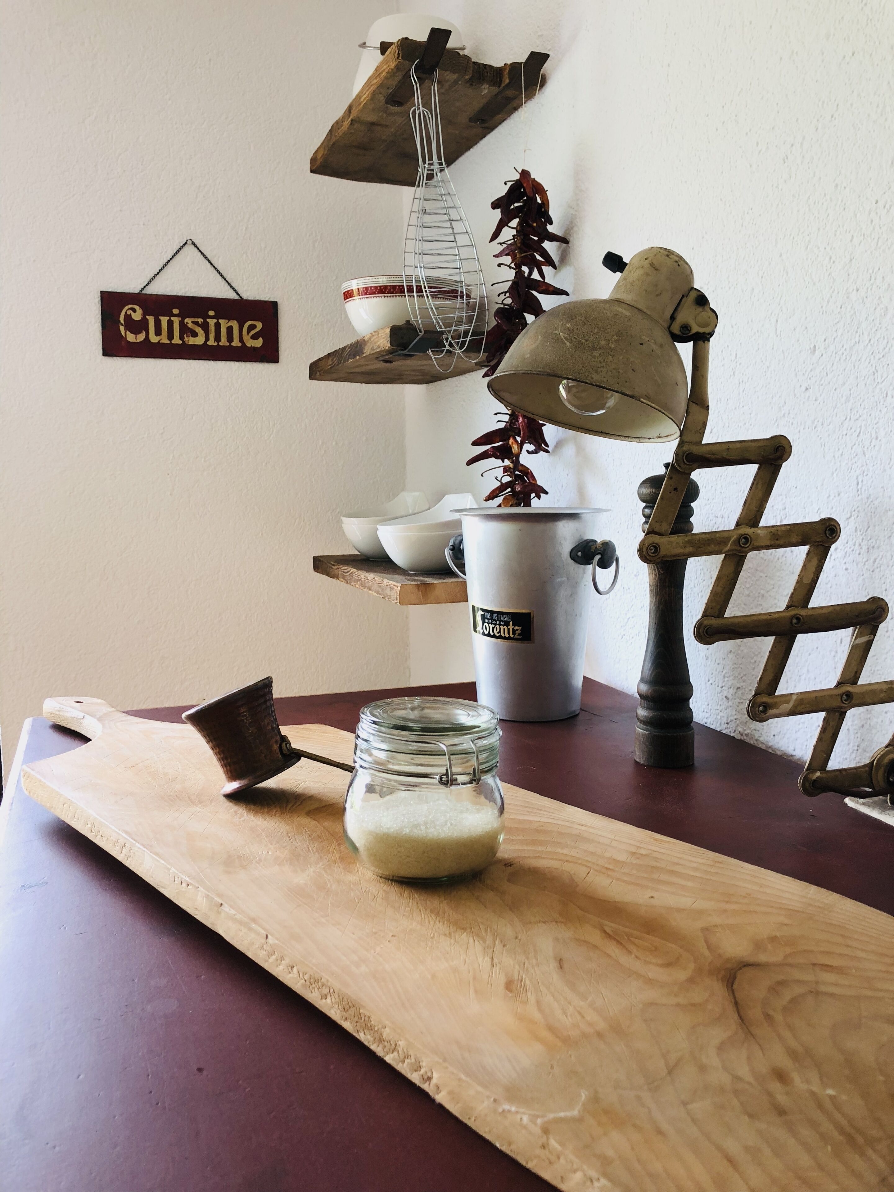 A wooden cutting board with a glass jar of white substance, a metal pot, and a vintage-style lamp on a table.