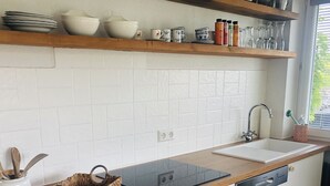 Una cocina con armarios blancos, encimera de madera, horno empotrado, lavavajillas y una ventana con persianas.