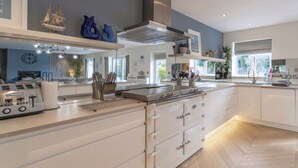 A modern kitchen with white cabinetry, a stainless steel range, and a central island with a built-in oven. - Drifters, Thornham, Norfolk (Thornham)