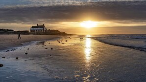 A beach with a building, a person walking, and the sun setting over the water. - Drifters, Thornham, Norfolk (Thornham)