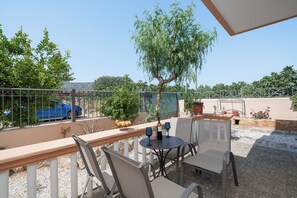 An outdoor patio with a table and chairs, surrounded by a gravel area and a metal fence. - Villa clotho (Markopoulo Mesogaias)