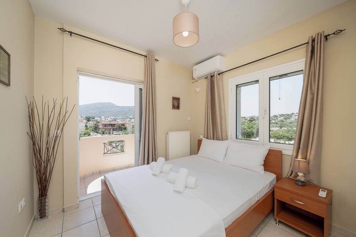 Une chambre d’hôtel avec un grand lit, une table de chevet avec une lampe, un radiateur et une vue sur la ville par les fenêtres.