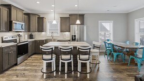 A modern kitchen with dark wood cabinets, a stainless steel refrigerator, a built-in microwave, and a large island with bar stools. - Perfectly SeaSun'd | Steps to Beach + Canal Front! (Surf City)