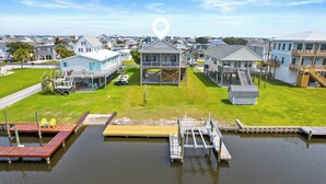 A waterfront property with a dock, a covered deck, and a grassy lawn. - Perfectly SeaSun'd | Steps to Beach + Canal Front! (Surf City)