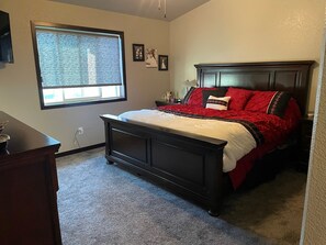 Une chambre avec un lit en bois foncé, une fenêtre avec des stores et une petite table de chevet.