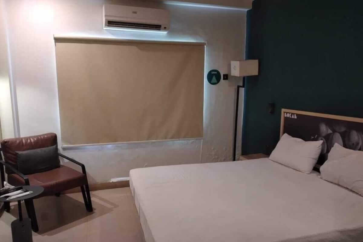 A hotel room with a bed, a chair, a desk, and a window with a blind.