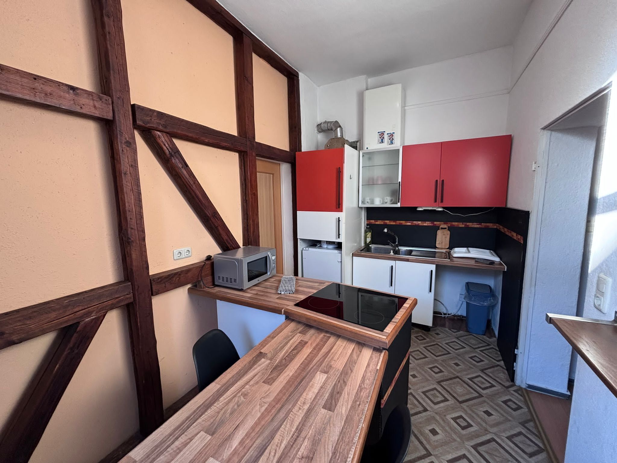A compact kitchen with a wooden table, a microwave, and red cabinets.