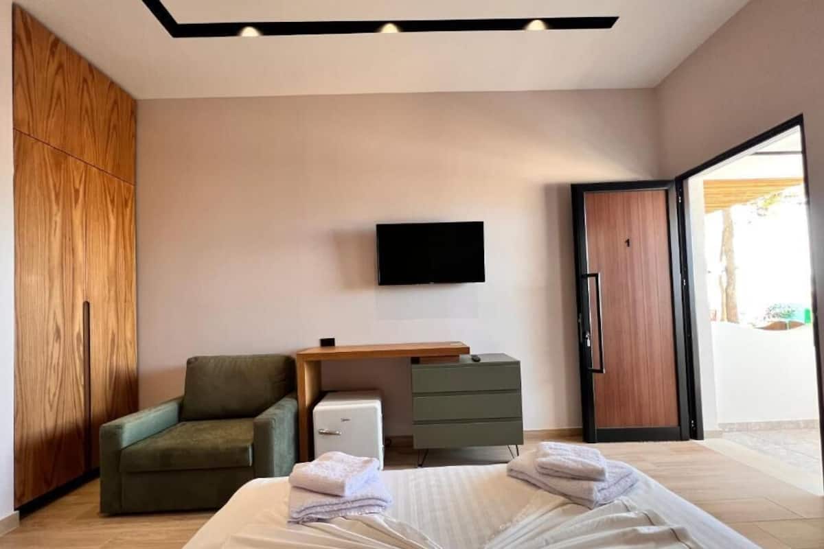 Une chambre à coucher moderne avec un lit, un bureau, une chaise, une télévision et une armoire.