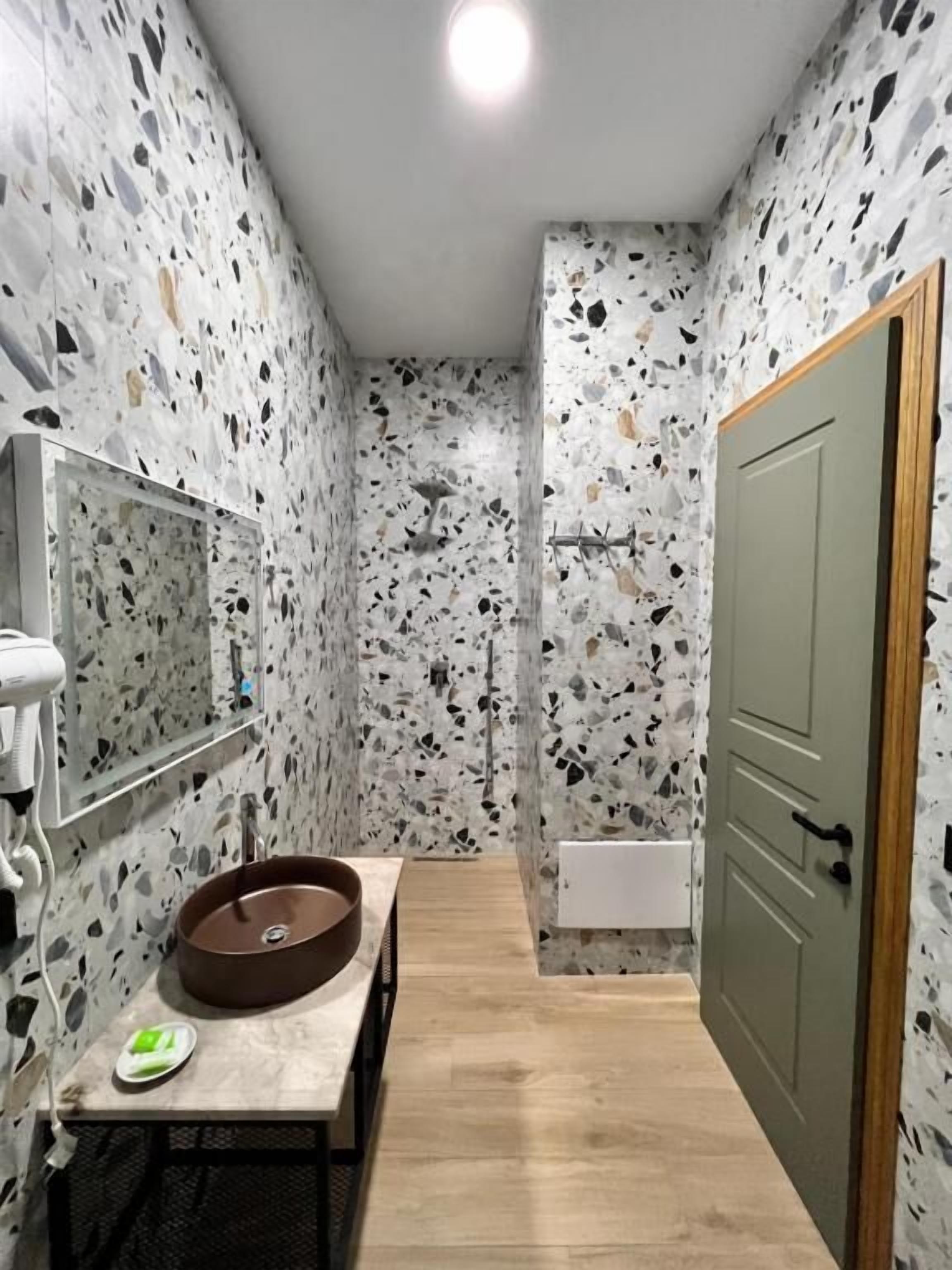 A bathroom with a terrazzo floor, a round sink, a mirror, and a shower.