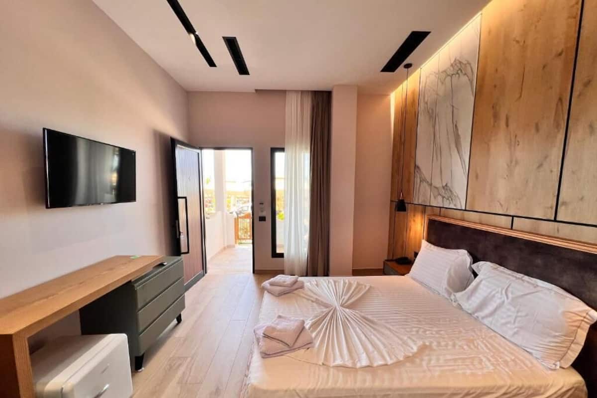 Une chambre d’hôtel moderne dotée d’un grand lit, d’un téléviseur à écran plat, d’un bureau en bois et offrant une vue sur l’extérieur.