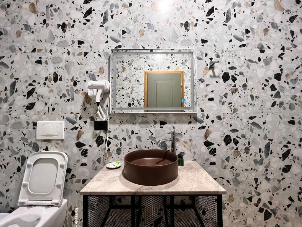 Un baño con piso de terrazo, un lavabo redondo, un inodoro y un espejo sobre el lavabo.
